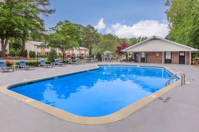 Outdoor swimming pool with lounge chairs and trees in the background.