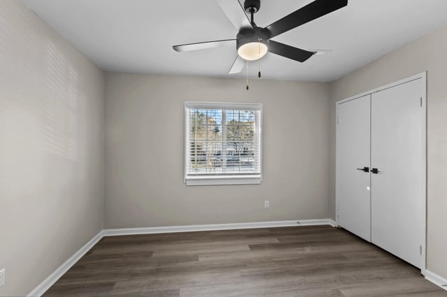 Empty bedroom with neutral walls, wood-look flooring, a ceiling fan, and a closet.
