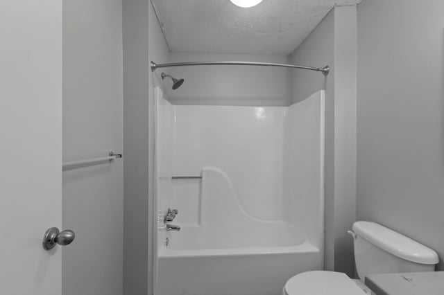 White bathtub with shower and toilet in a neutral-toned bathroom.