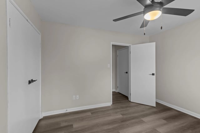 Empty bedroom with white doors, ceiling fan, and wood-look flooring.