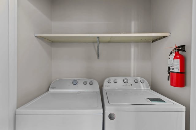 Whirlpool washer and dryer set with a shelf above and a fire extinguisher on the side.