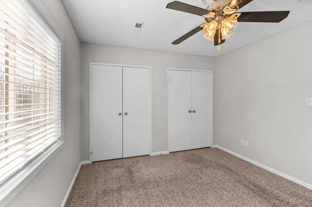 Bedroom with two closets, a ceiling fan, and a window with blinds.