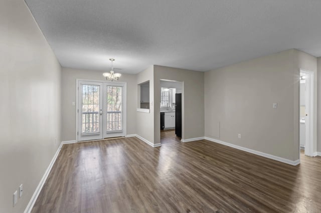 Empty living and dining room with wood floors and a view of the kitchen.