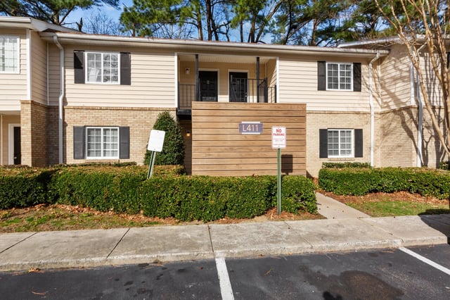 Exterior of apartment building with beige siding and brick accents, featuring multiple windows and doors.