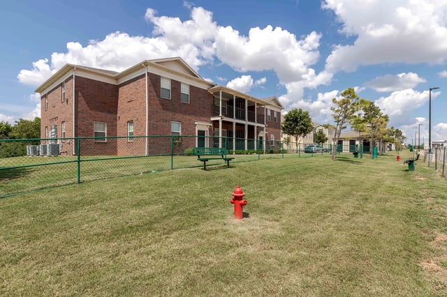 Exterior view of apartment buildings with a fenced dog park area in the foreground.