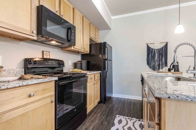 Modern kitchen with light wood cabinets, black appliances, and granite countertops.