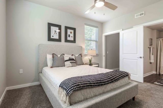 Queen-size bed with patterned pillows and throw blanket in a neutral-toned bedroom.