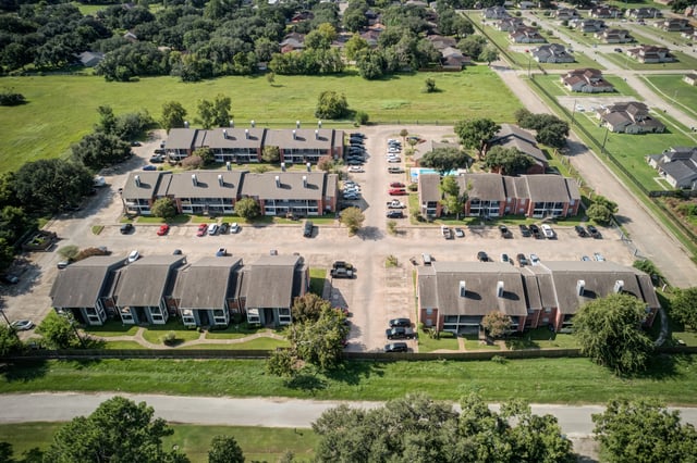 Aerial view of apartment buildings with parking lots and surrounding greenery.