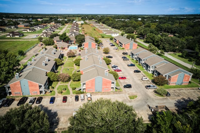 Aerial view of apartment buildings with a pool and parking lots.