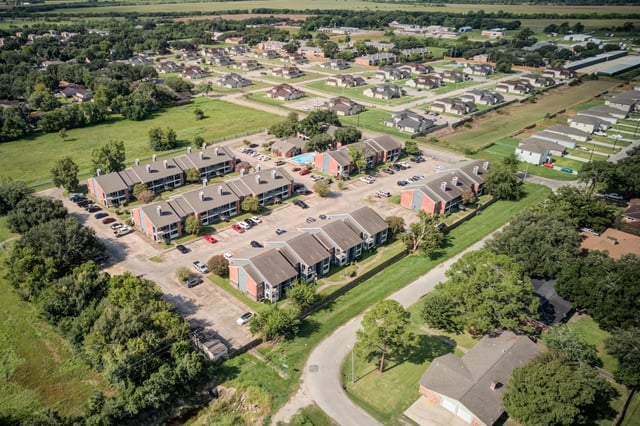 Aerial view of apartment buildings with a pool and surrounding landscaping.