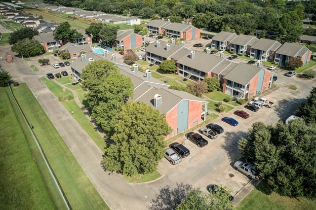 Aerial view of apartment buildings with a pool and parking lot.