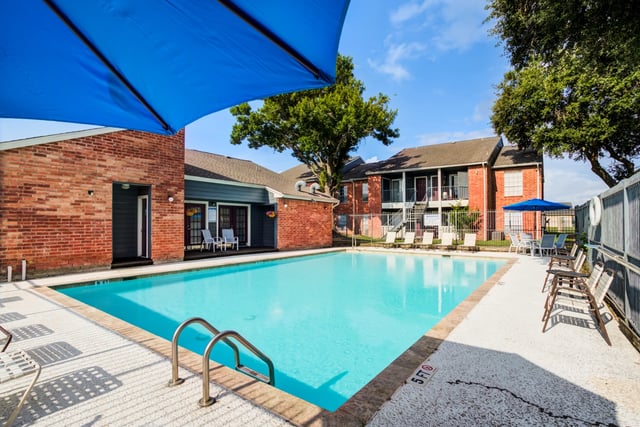 Refreshing swimming pool with lounge chairs and umbrellas, surrounded by apartment buildings.