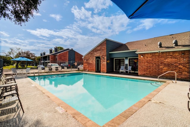 Swimming pool with lounge chairs and umbrellas, apartment buildings in the background.