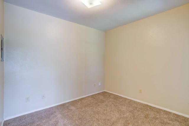 Empty room with neutral-colored walls and carpet flooring. Features include a ceiling light fixture and electrical outlets.