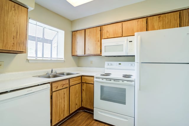 Kitchen with wood cabinets, white countertops, sink, dishwasher, stove, and microwave.