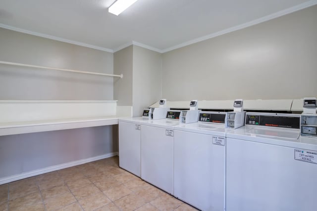 Commercial washers and dryers in a laundry room with a folding counter.