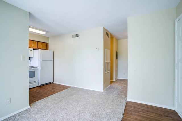 Interior view of an apartment kitchen and living area with carpet and wood-look flooring.
