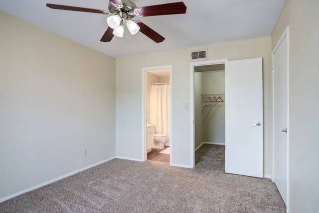Bedroom with a ceiling fan and a view into a bathroom and a closet.
