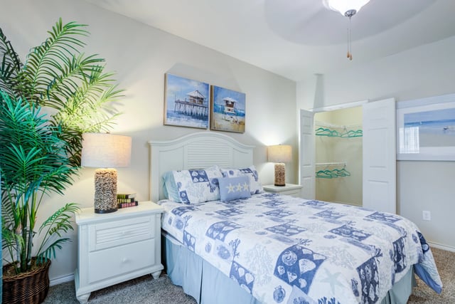 Queen size bed with coastal-themed bedding in a bedroom with a large closet and palm plant.
