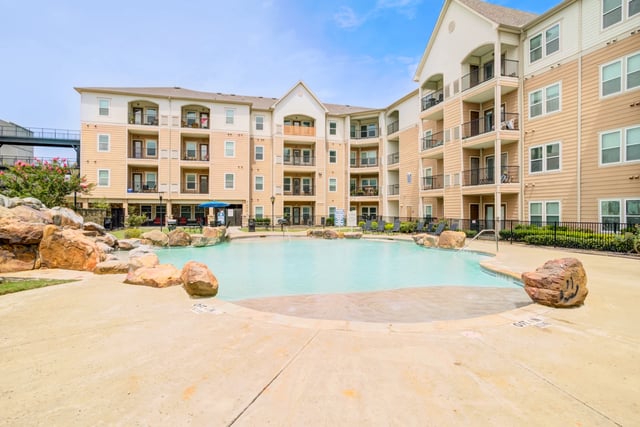 Outdoor swimming pool with lounge chairs and apartment buildings in the background.