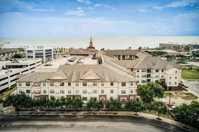 Aerial view of apartment buildings with a parking garage and the ocean in the background.