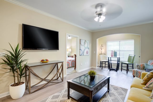 Living room with a TV, console table, coffee table, dining area, and entrance to bedroom.