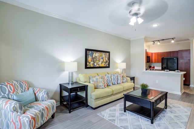 Living room with a yellow sofa, patterned armchair, and kitchen in the background.