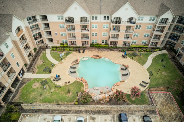 Aerial view of an apartment complex courtyard with a free-form swimming pool and surrounding buildings.