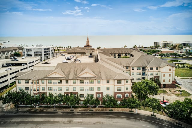 Aerial view of a multi-building apartment complex with a water view and parking garage.