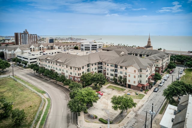 Aerial view of a large apartment complex with multiple buildings, overlooking the ocean.