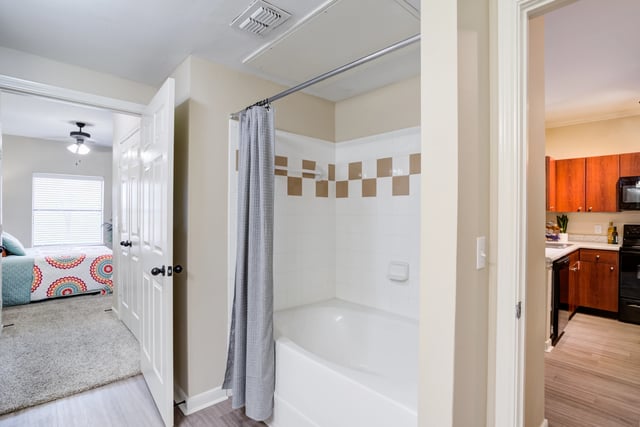 Bathroom with a bathtub and shower curtain, and a glimpse of a bedroom and kitchen.