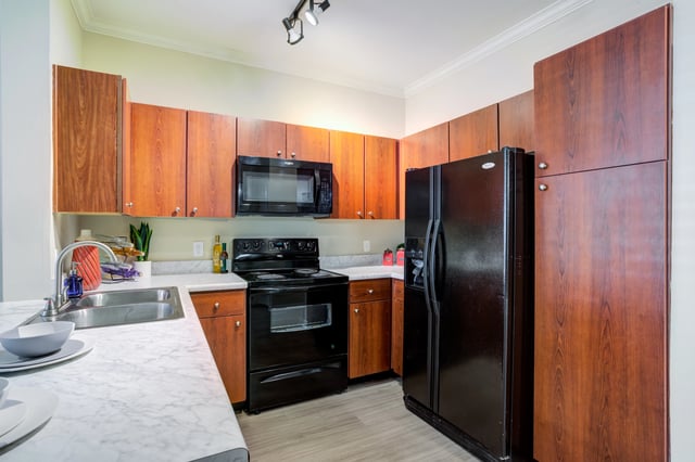 Kitchen with dark wood cabinets, black appliances, and marble countertops.