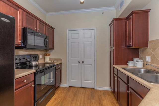 Kitchen with cherry wood cabinets, black appliances, and double doors.