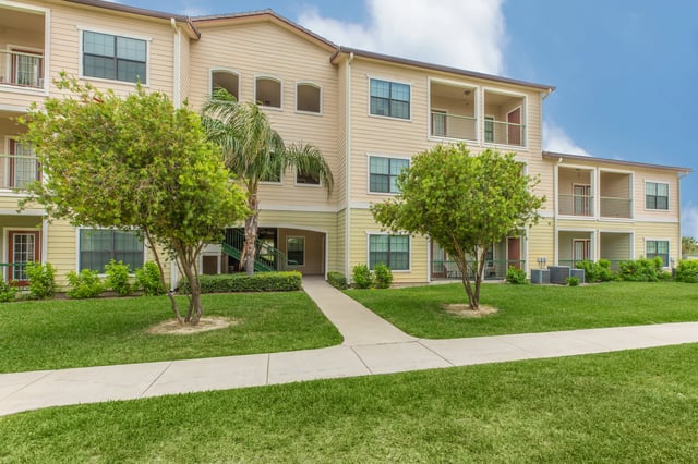 Exterior view of a multi-story apartment building with balconies and manicured grounds.