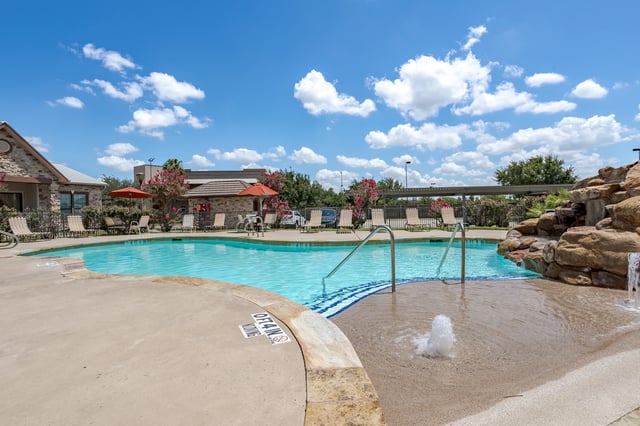 Outdoor swimming pool with a rock waterfall feature and lounge chairs.
