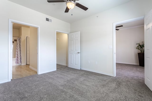 View of a bedroom with carpet and a ceiling fan, looking into a bathroom and a closet.