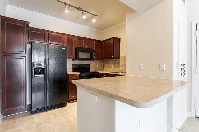 Modern kitchen with dark wood cabinets, black appliances, and a breakfast bar.