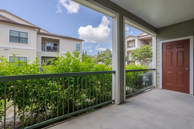 View of apartment buildings from a covered patio with lush greenery and a blue sky.