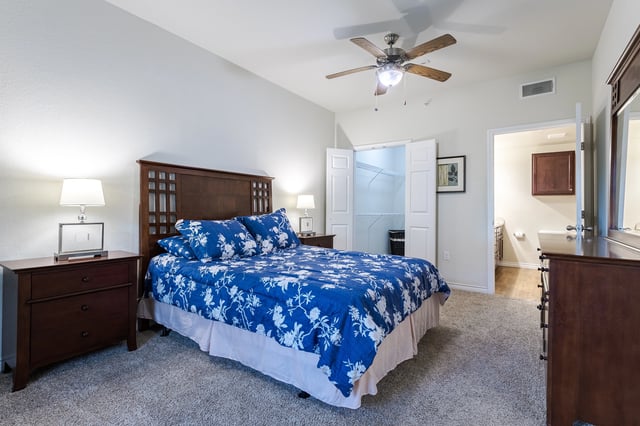 Bedroom with king size bed and blue floral comforter, nightstand, dresser, and walk-in closet.