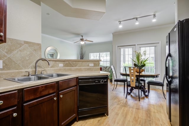 Kitchen and dining area with dark wood cabinets, stainless steel sink, black dishwasher and refrigerator, and a round dining table with chairs.