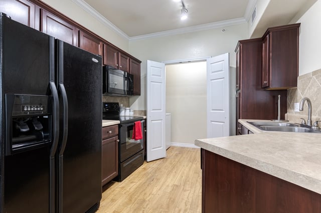 Modern kitchen with dark wood cabinets, black appliances, and light wood flooring.