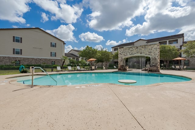 Outdoor swimming pool with a stone waterfall feature and lounge chairs.