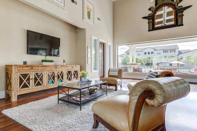 Lounge area with seating, coffee table, and TV, overlooking the community pool area.
