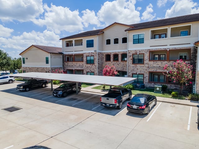 Apartment building exterior with covered parking and manicured landscaping.