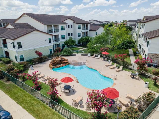 Apartment complex swimming pool area with lounge chairs, tables, and umbrellas.