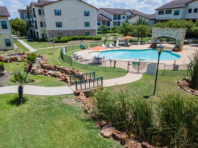 Apartment complex courtyard with a swimming pool, lounge chairs, and umbrellas.