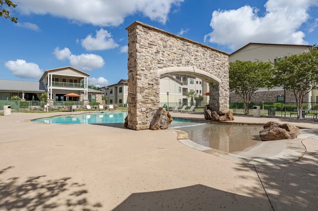 Outdoor swimming pool area with a stone water feature and lounge chairs.