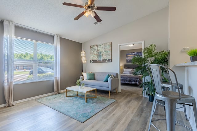Living room with gray sofa, coffee table, and rug, leading into a bedroom with a bed.