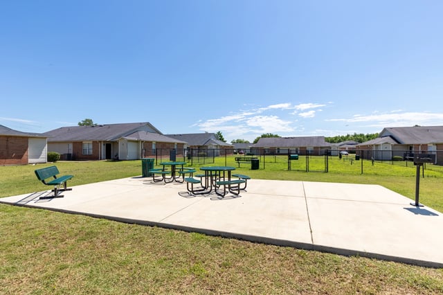 Picnic tables, benches, and grills in an outdoor common area with apartment buildings in the background.