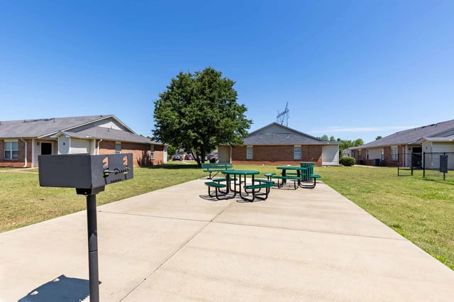Outdoor picnic area with grill and picnic tables at apartment complex.